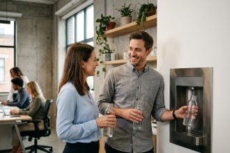 Deux employés de bureau remplissant leurs gourdes à une fontaine à eau raccordée au réseau dans un espace de travail moderne